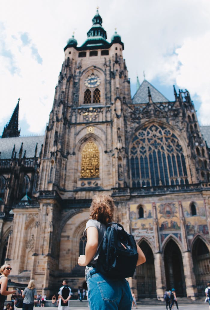 Traveler admires the stunning facade of St. Vitus Cathedral in Prague, under a bright sky.